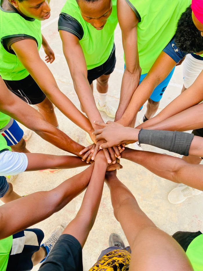 A diverse group of athletes join hands in unity during an outdoor sports session.
